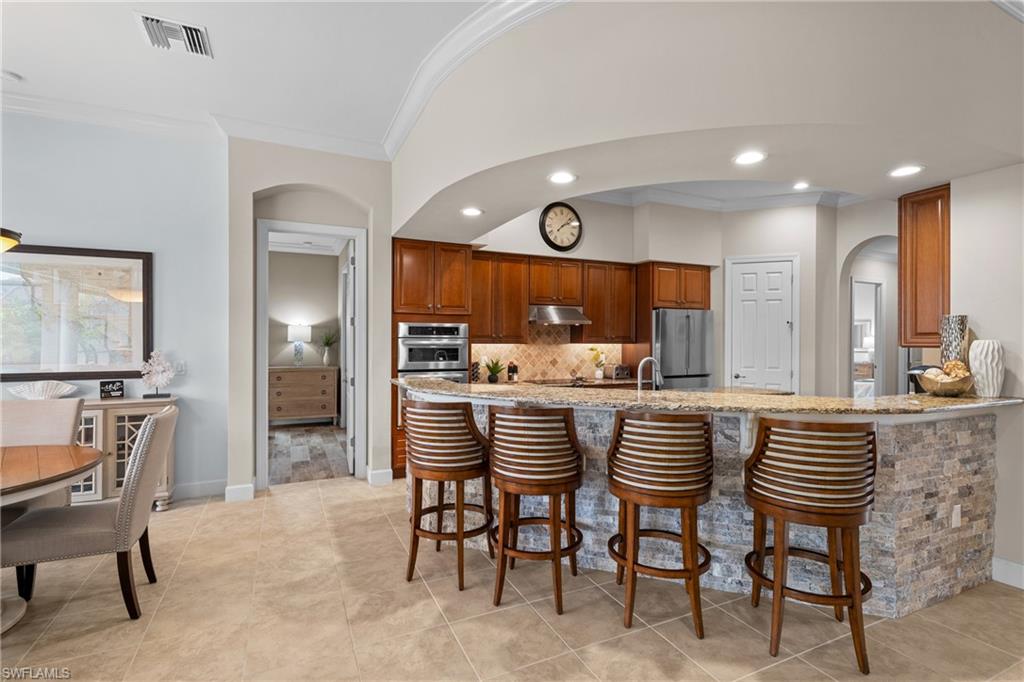 Kitchen featuring a breakfast bar area, arched walkways, a peninsula, light stone countertops, and wood finish cabinets