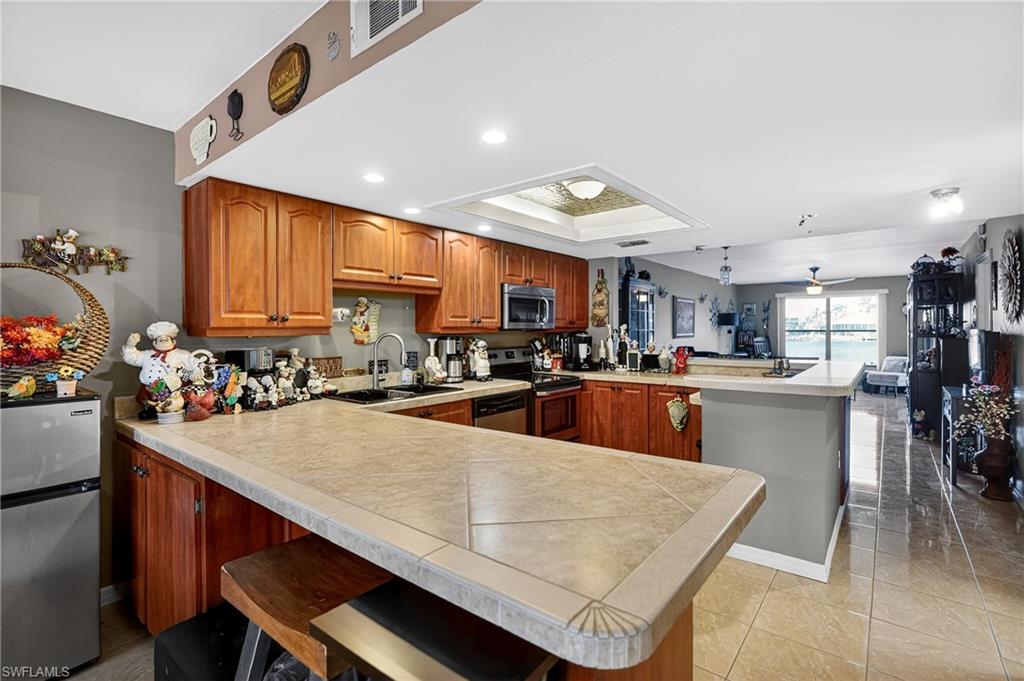 Kitchen featuring a peninsula, wood finish cabinets, a kitchen bar, stainless steel appliances, and a tray ceiling