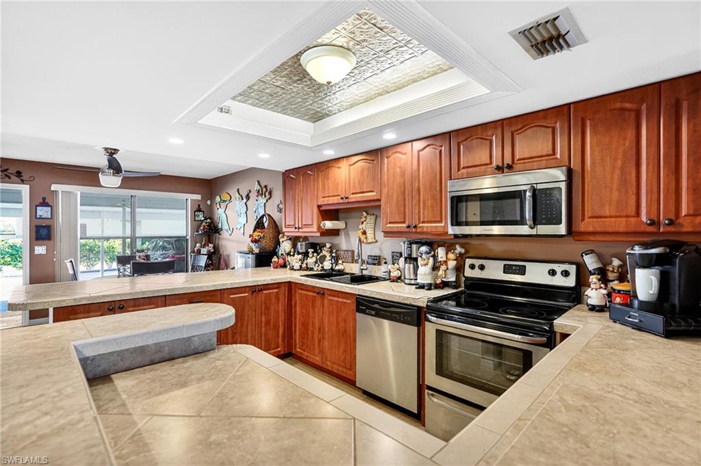 Kitchen featuring a tray ceiling, wood finish cabinets, stainless steel appliances, recessed lighting, and a peninsula