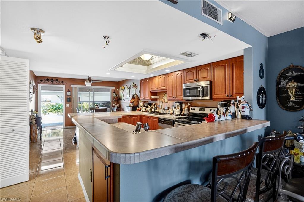 Kitchen featuring a peninsula, a breakfast bar, wood finish cabinetry, stainless steel appliances, and a tray ceiling