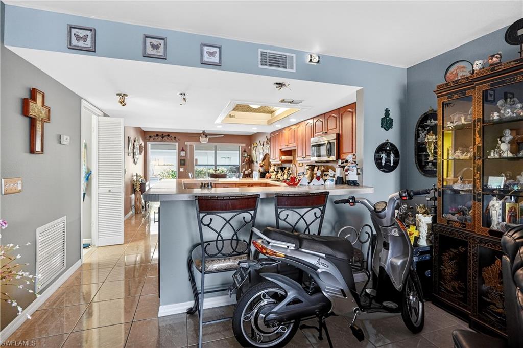 Kitchen with a tray ceiling, a peninsula, stainless steel microwave, light countertops, and a breakfast bar
