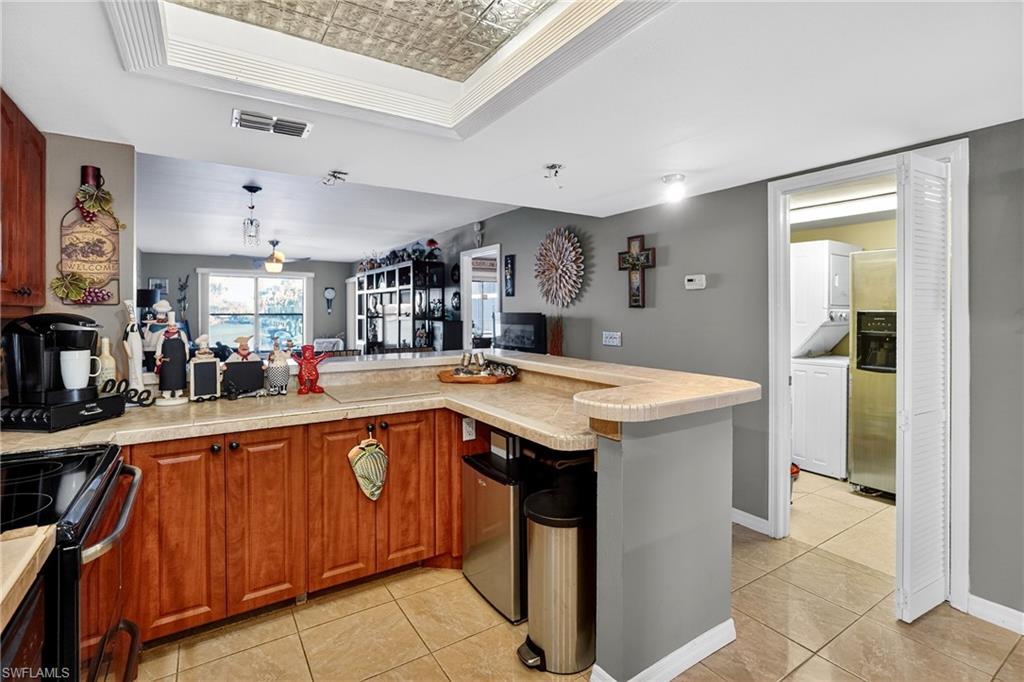 Kitchen featuring an ornate ceiling, a peninsula, black electric range oven, light tile patterned floors, and a raised ceiling
