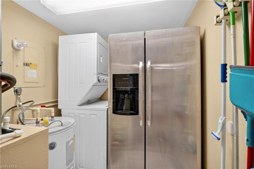 Laundry area with electric panel, stacked washer and clothes dryer, and water heater