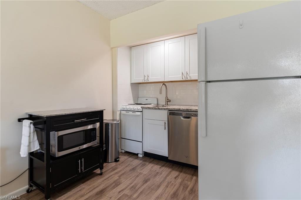 Kitchen with stainless steel appliances, white cabinetry, light wood-style flooring, light stone countertops, and tasteful backsplash