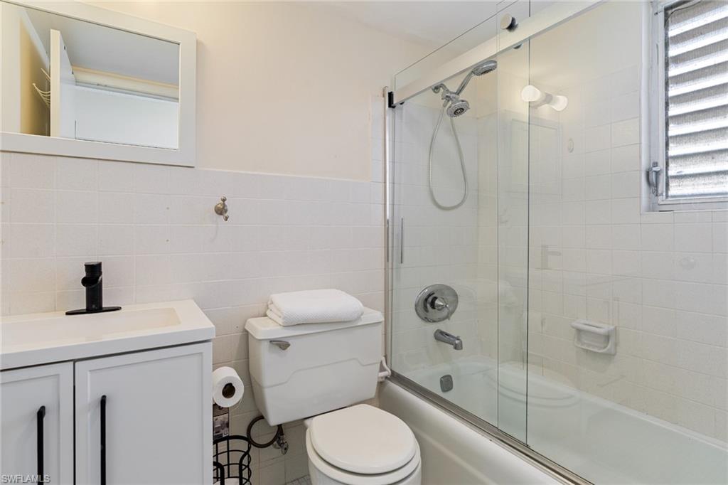 Full bathroom with vanity, tile walls, combined bath / shower with glass door, and wainscoting
