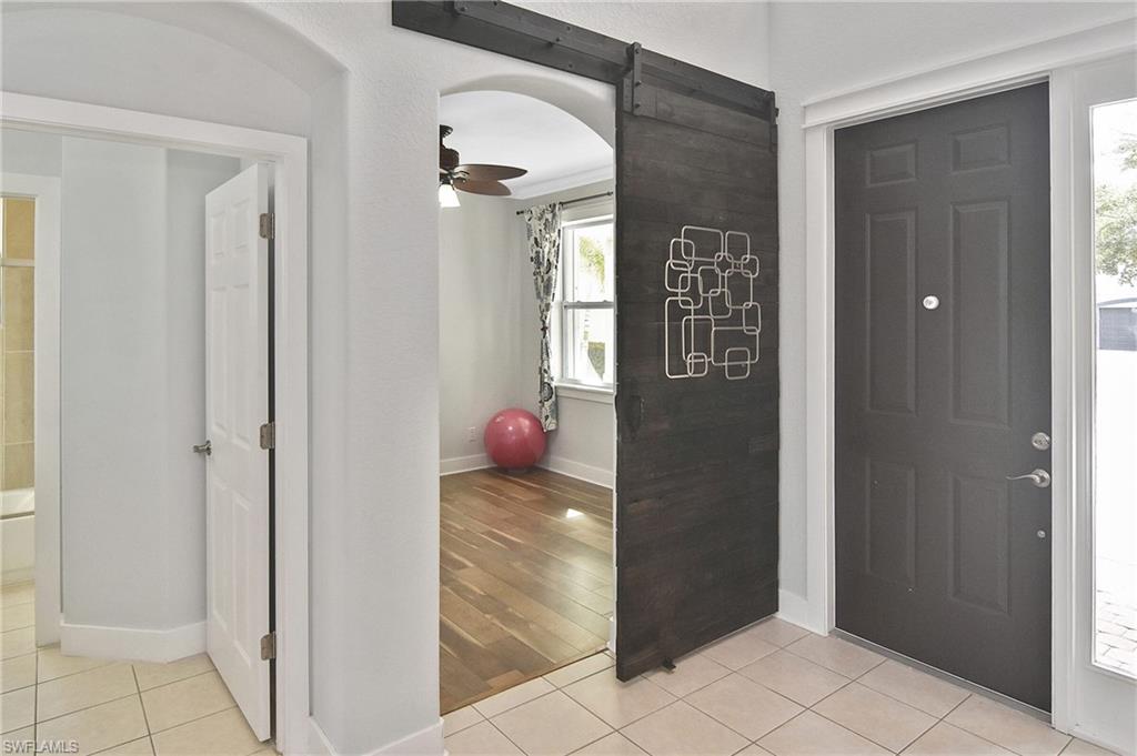 Foyer entrance with ceiling fan, a barn door, light tile patterned flooring, and arched walkways