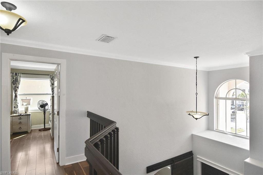 Hall featuring dark wood-style floors, ornamental molding, and an upstairs landing