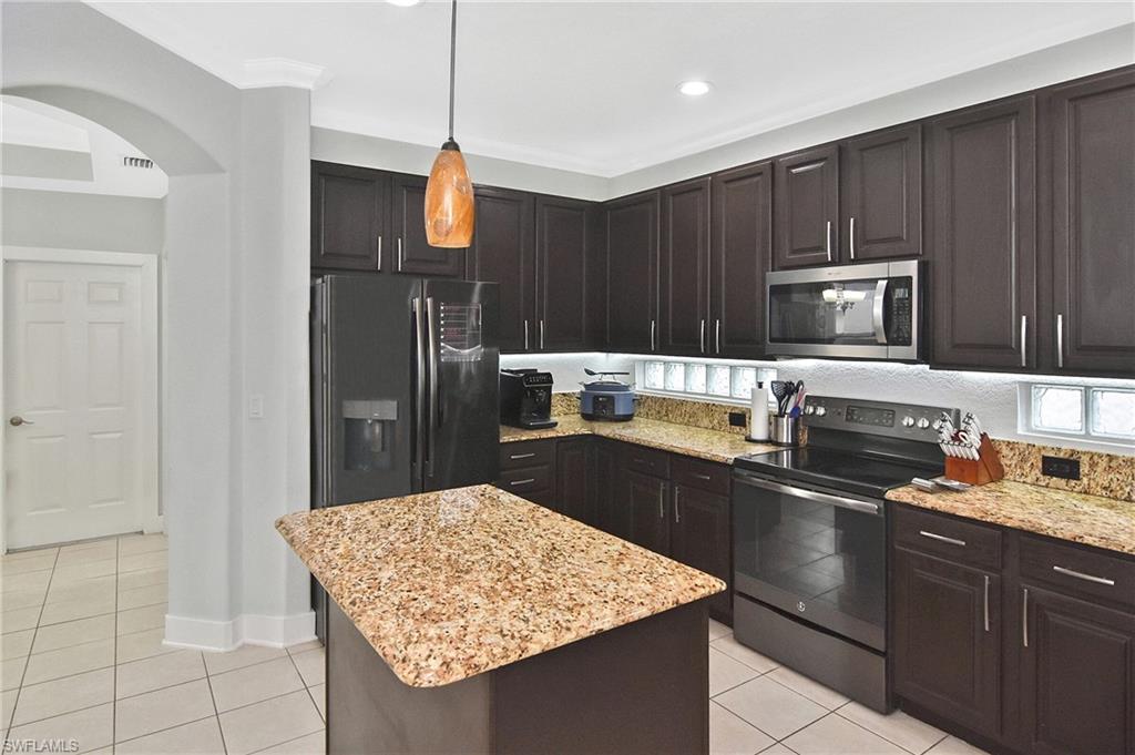 Kitchen featuring range with electric cooktop, dark wood finish cabinetry, stainless steel microwave, and light tile patterned floors