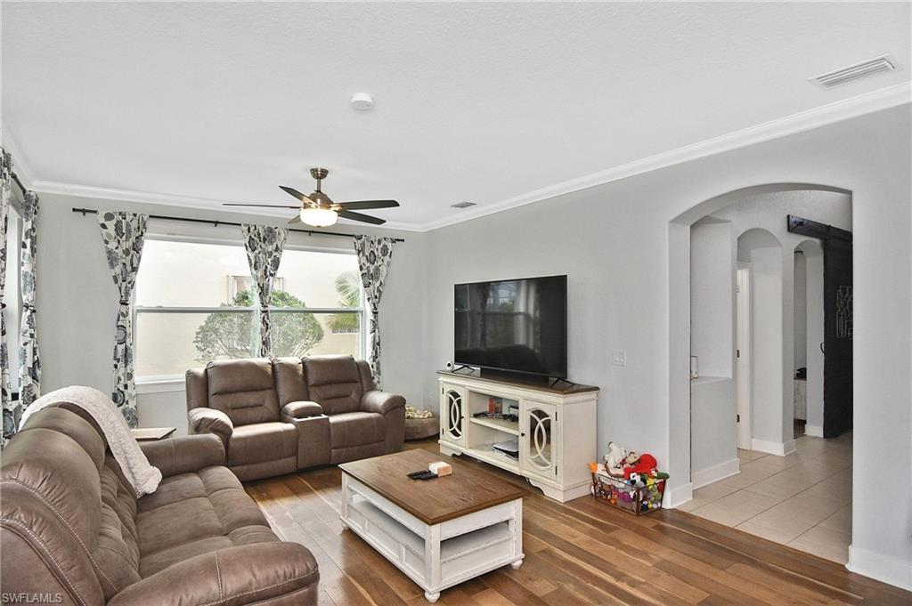 Living area featuring ornamental molding, arched walkways, light wood finished floors, and ceiling fan