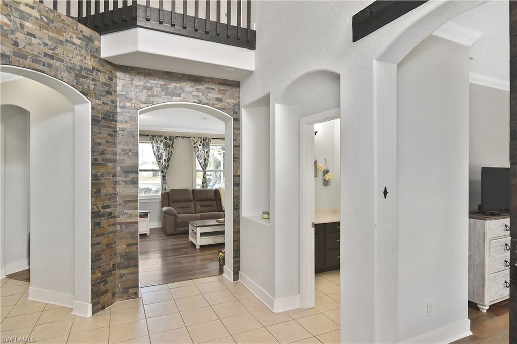 Corridor with arched walkways, light tile patterned flooring, and crown molding