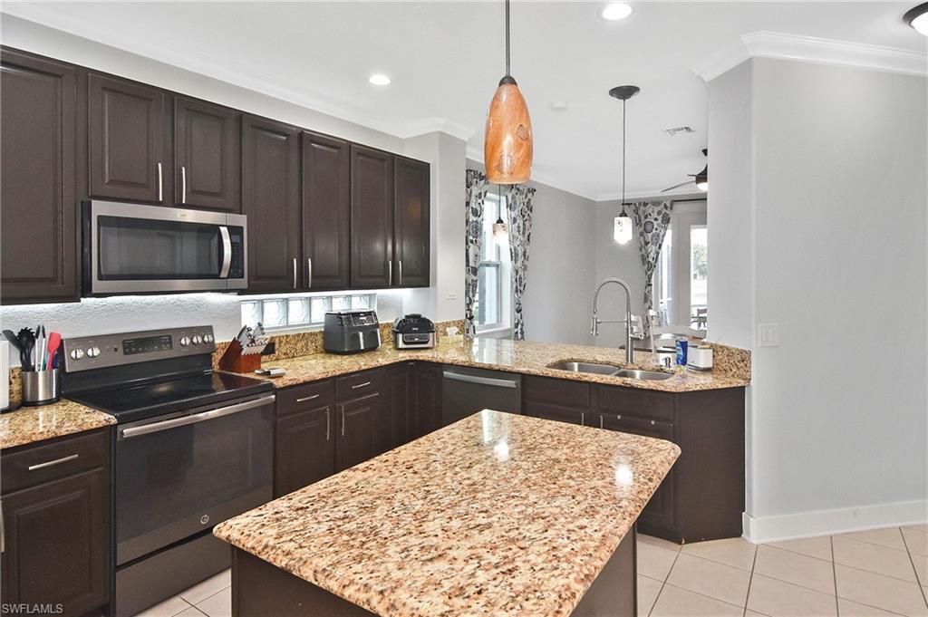 Kitchen featuring stainless steel appliances, dark wood finish cabinets, light stone countertops, crown molding, and decorative light fixtures
