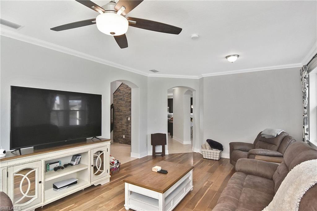 Living area featuring crown molding, arched walkways, light wood-style floors, and a ceiling fan