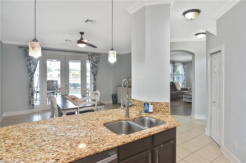 Kitchen with light tile patterned flooring, ornamental molding, light stone counters, ceiling fan, and pendant lighting