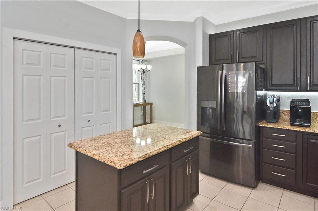 Kitchen with stainless steel fridge with ice dispenser, hanging light fixtures, a center island, light stone countertops, and crown molding