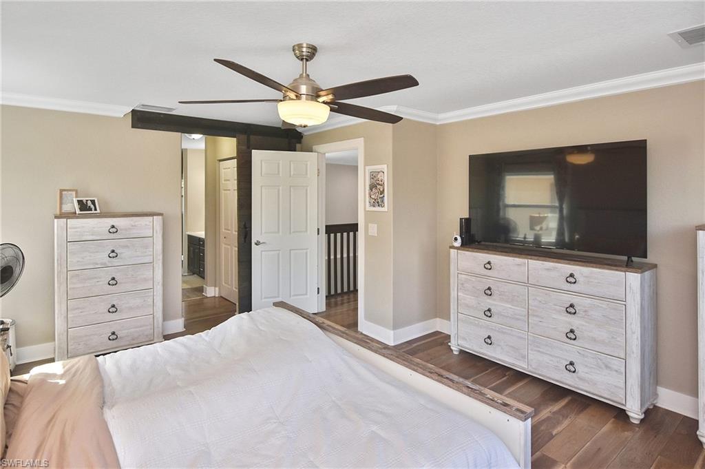 Bedroom with crown molding, a ceiling fan, dark wood-type flooring, and ensuite bath