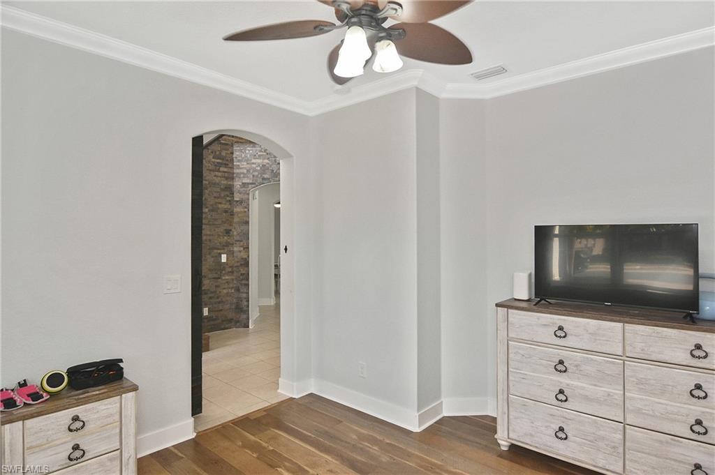 Bedroom featuring arched walkways, crown molding, dark wood-style floors, and a ceiling fan