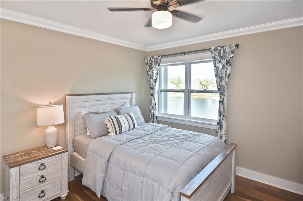Bedroom with dark wood-type flooring, a water view, crown molding, and a ceiling fan