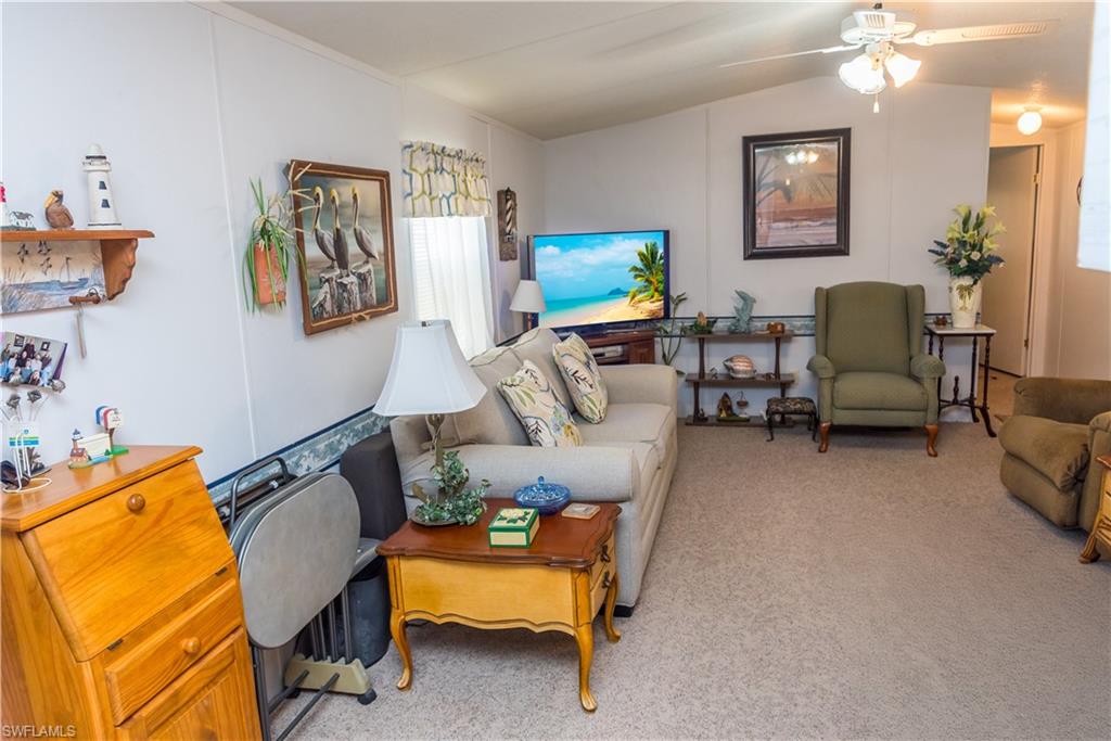 Living room with light colored carpet, ceiling fan, and lofted ceiling