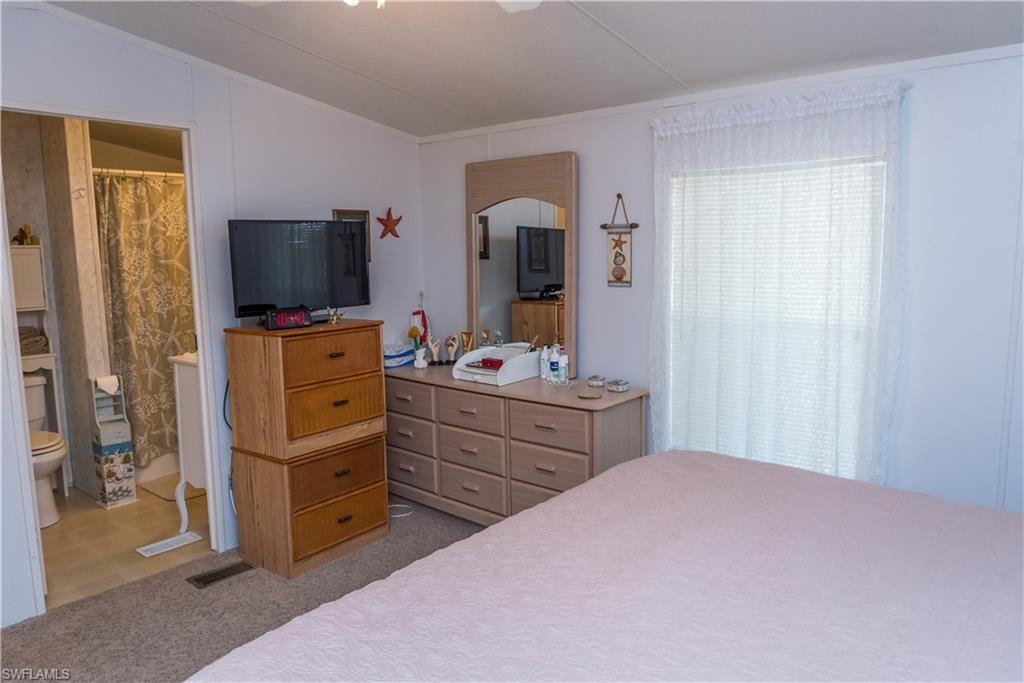 Bedroom with vaulted ceiling, ensuite bath, a ceiling fan, and light colored carpet