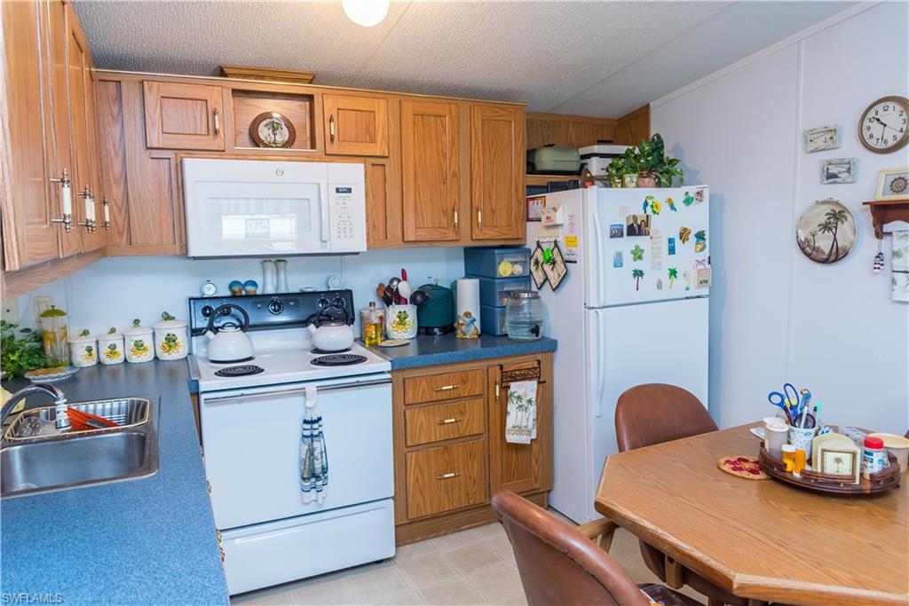 Kitchen with white appliances, wood finish cabinetry, dark countertops, light flooring, and a textured ceiling