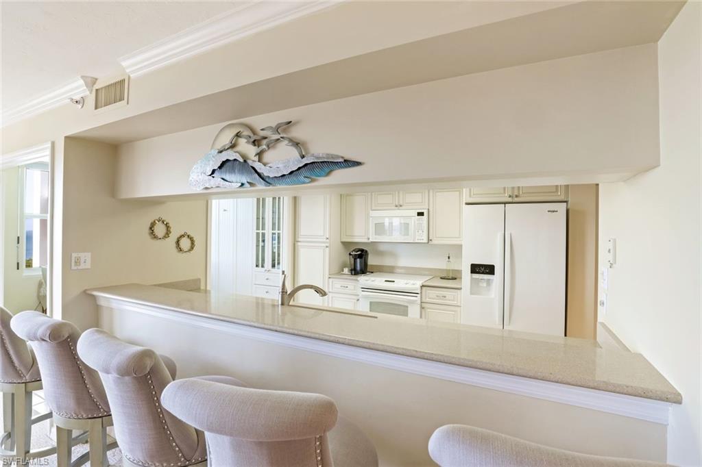 Kitchen featuring a peninsula, white appliances, crown molding, a kitchen bar, and light stone countertops