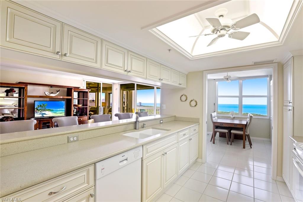 Kitchen with a ceiling fan, white appliances, a skylight, cream cabinets, and light tile patterned flooring
