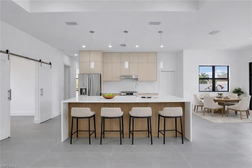 Kitchen featuring a barn door, a spacious island, decorative light fixtures, stainless steel appliances, and a kitchen breakfast bar. This photo was digitally staged.