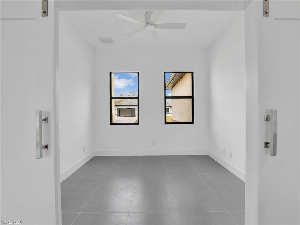 Unfurnished room with a barn door, light tile patterned flooring, and a ceiling fan