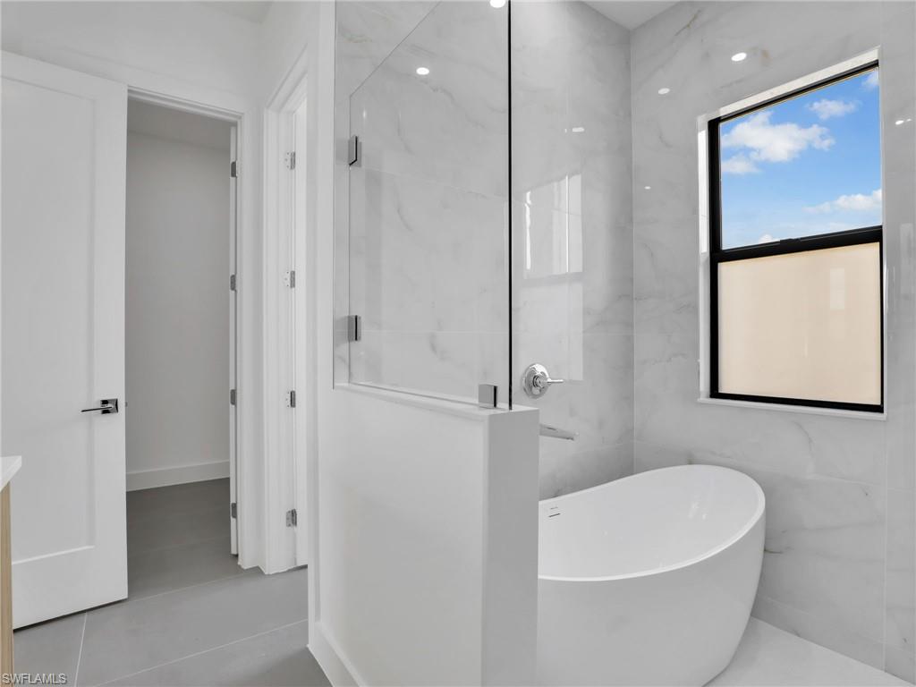 Bathroom featuring a freestanding tub, a marble finish shower, and vanity