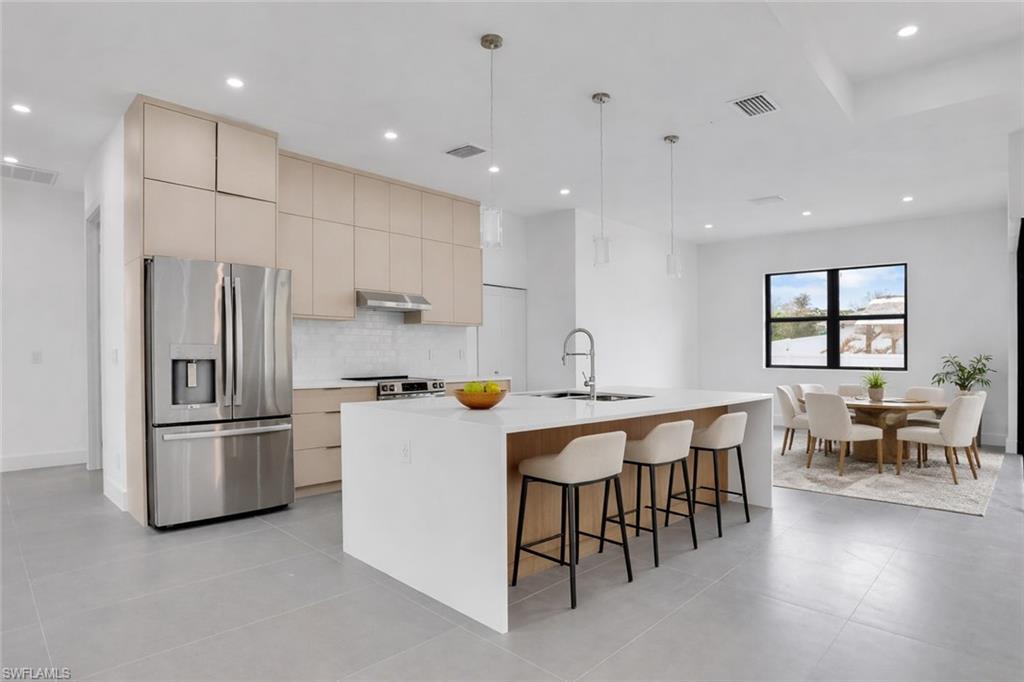Kitchen with stainless steel appliances, an island with sink, decorative light fixtures, a breakfast bar, and light stone countertops. This photo was digitally staged.