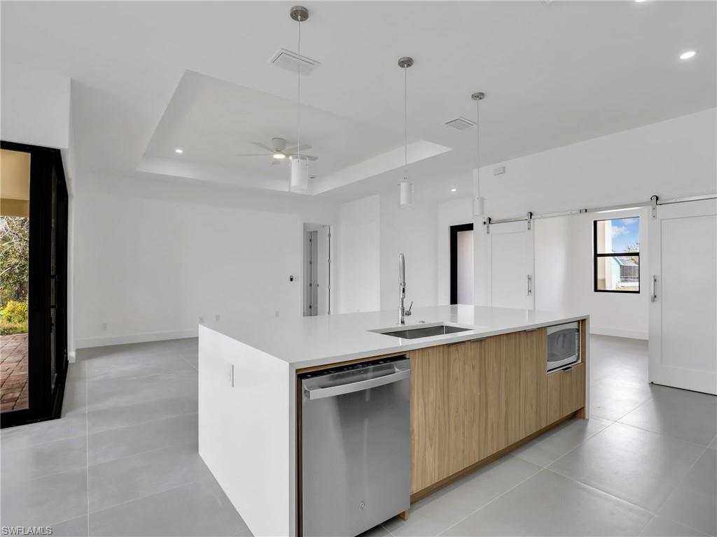Kitchen with modern cabinets, an island with sink, stainless steel appliances, a barn door, and light stone countertops