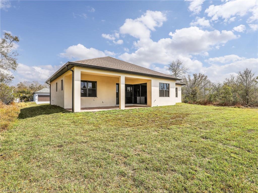 Rear view of house with stucco siding, a yard, and a patio area