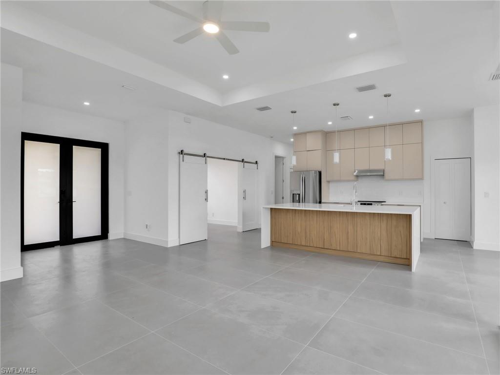 Kitchen featuring a barn door, a large island with sink, open floor plan, stainless steel fridge, and decorative light fixtures