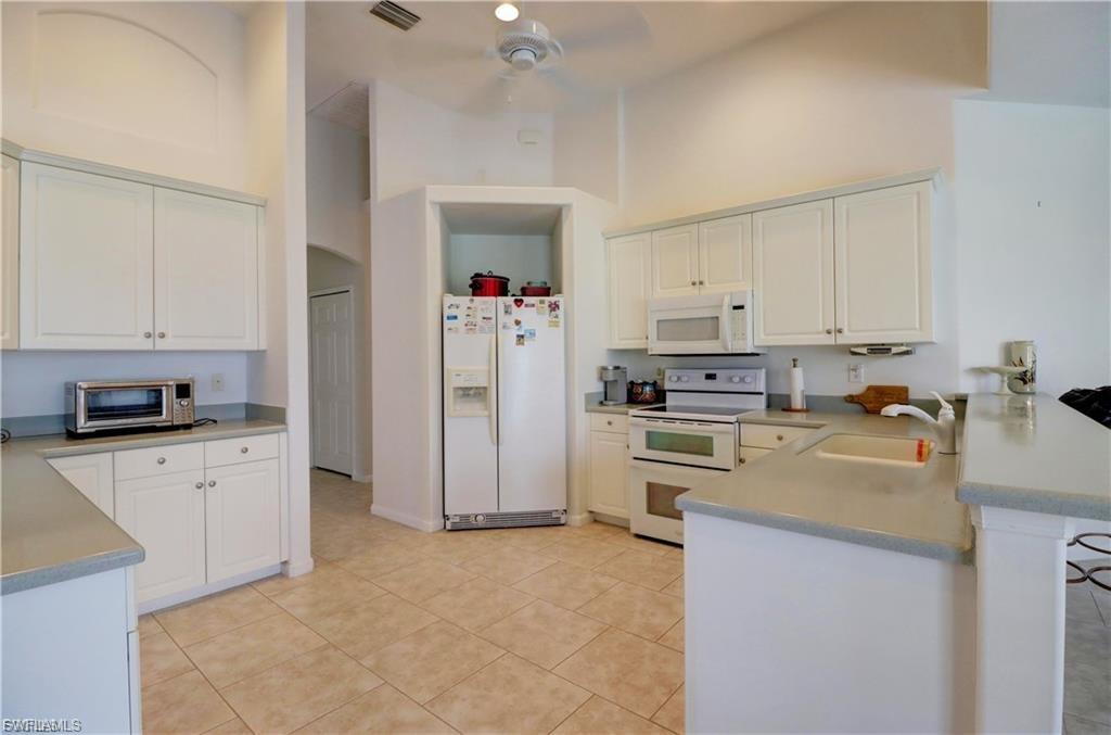 Kitchen featuring a peninsula, a high ceiling, white appliances, light countertops, and a kitchen bar