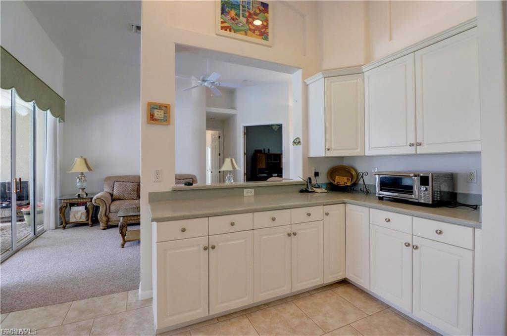 Kitchen with light countertops, light carpet, white cabinets, ceiling fan, and a high ceiling