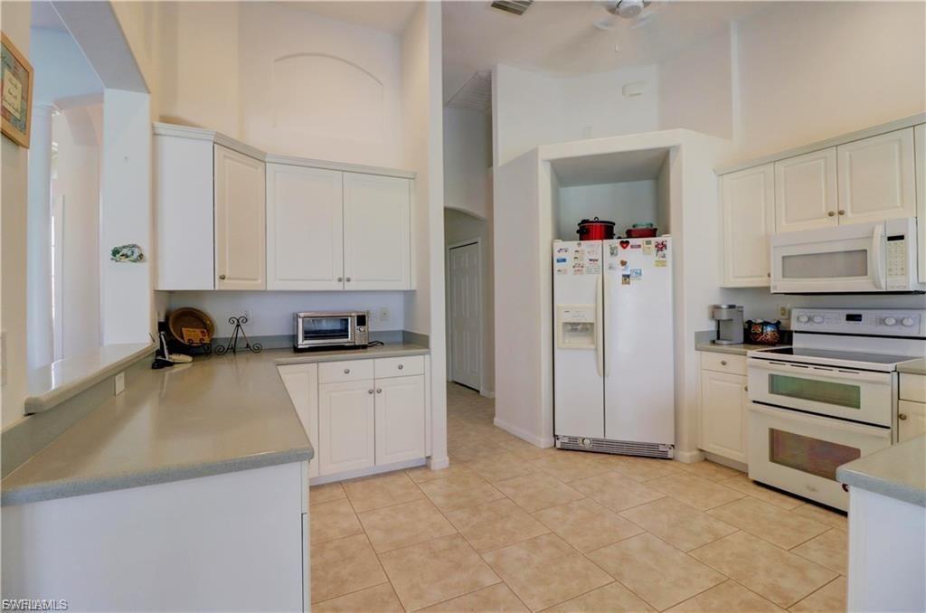 Kitchen with white appliances, a high ceiling, white cabinets, light countertops, and ceiling fan