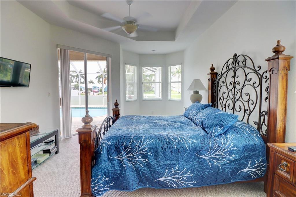Bedroom with a tray ceiling, light carpet, access to outside, and ceiling fan