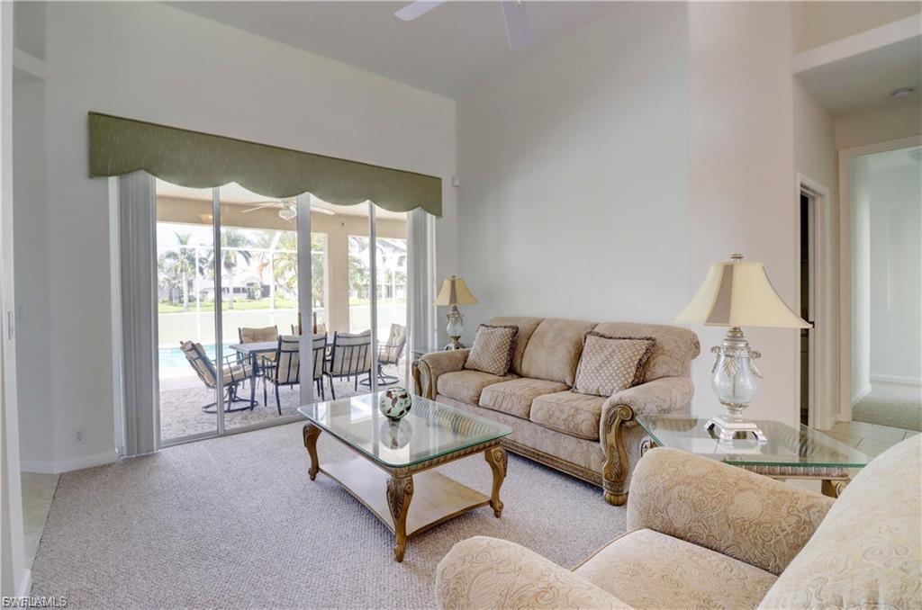 Living room featuring light carpet, a sunroom, a ceiling fan, and a high ceiling