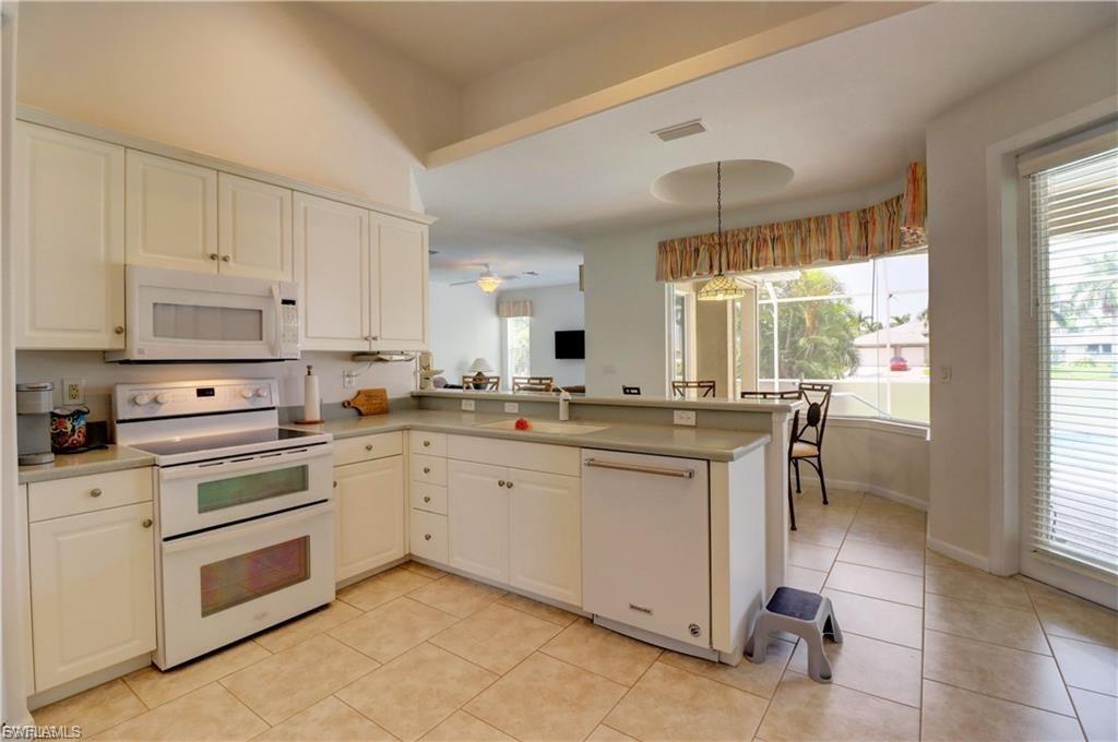 Kitchen featuring white appliances, a peninsula, hanging light fixtures, light countertops, and white cabinets