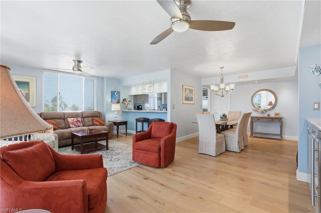 Living room featuring a ceiling fan, light wood-type flooring, and suspended lighting - Virtually Edited Image