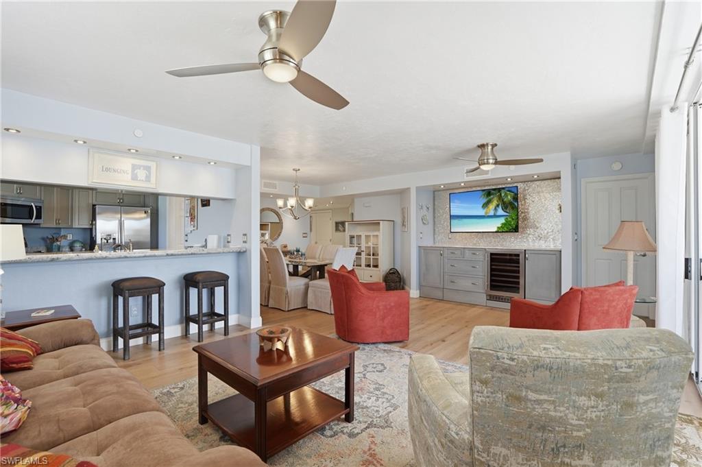 Living room featuring hanging lights, light wood-style flooring, beverage cooler, and a ceiling fan - Virtually Edited Image