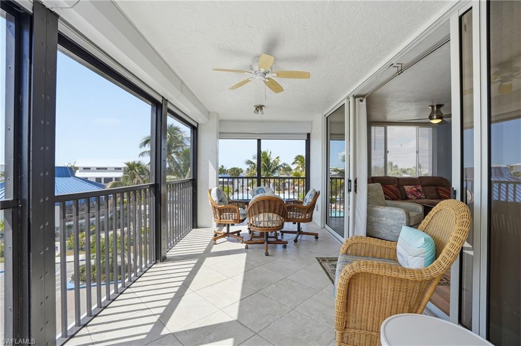 Sunroom / solarium featuring ceiling fan, a textured ceiling, a balcony, and tile patterned flooring - Virtually Edited Image