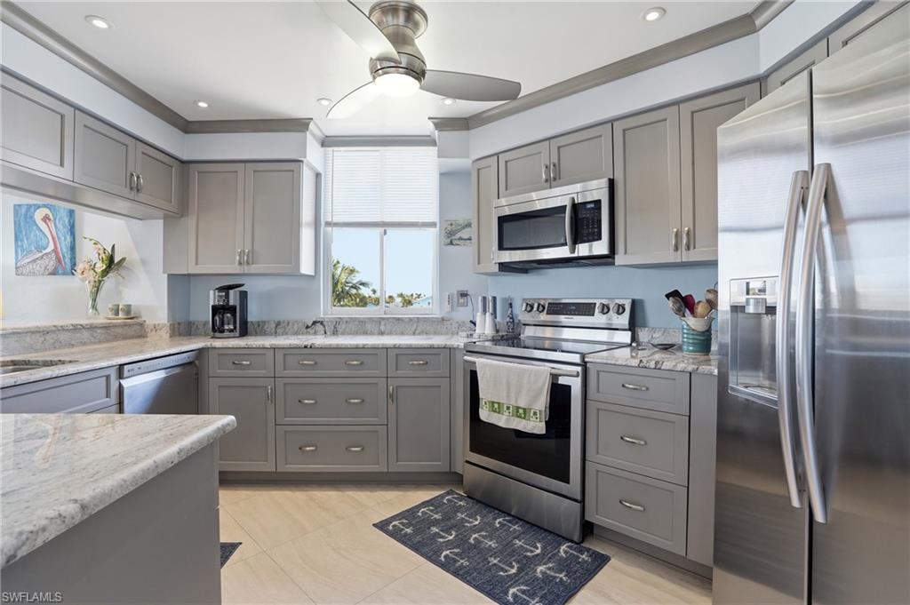 Kitchen with gray cabinetry, stainless steel appliances, light stone counters, ornamental molding, and ceiling fan - Virtually Edited Image
