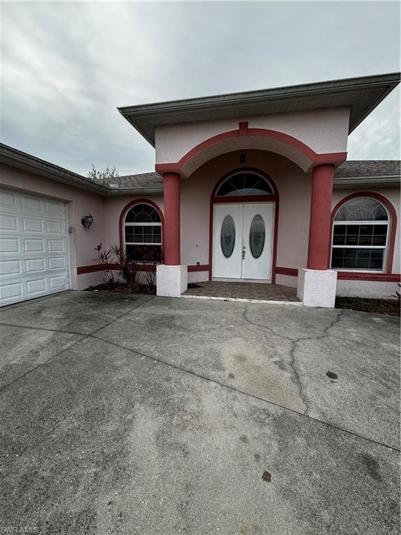 Property entrance featuring an attached garage, stucco siding, driveway, and roof with shingles