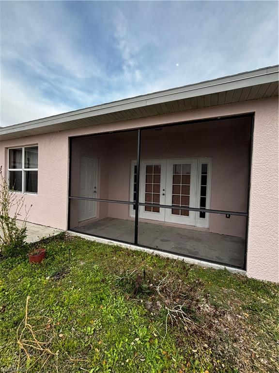 Rear view of property featuring french doors, stucco siding, and a sunroom