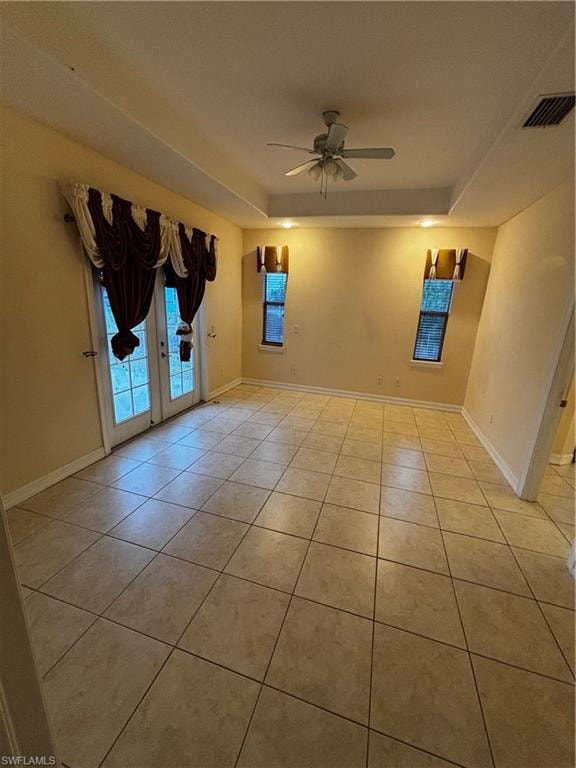 Unfurnished room featuring a raised ceiling, a ceiling fan, light tile patterned flooring, and french doors