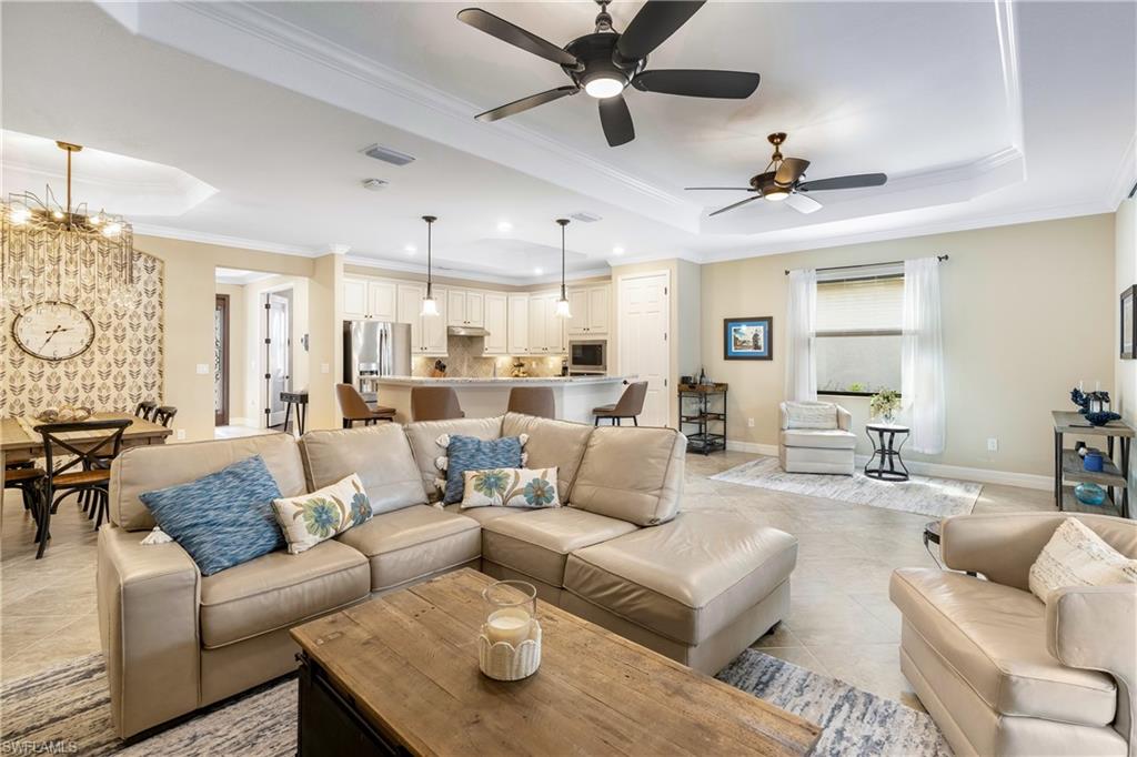 Living area featuring crown molding, suspended lighting, a raised ceiling, a ceiling fan, and light tile patterned floors