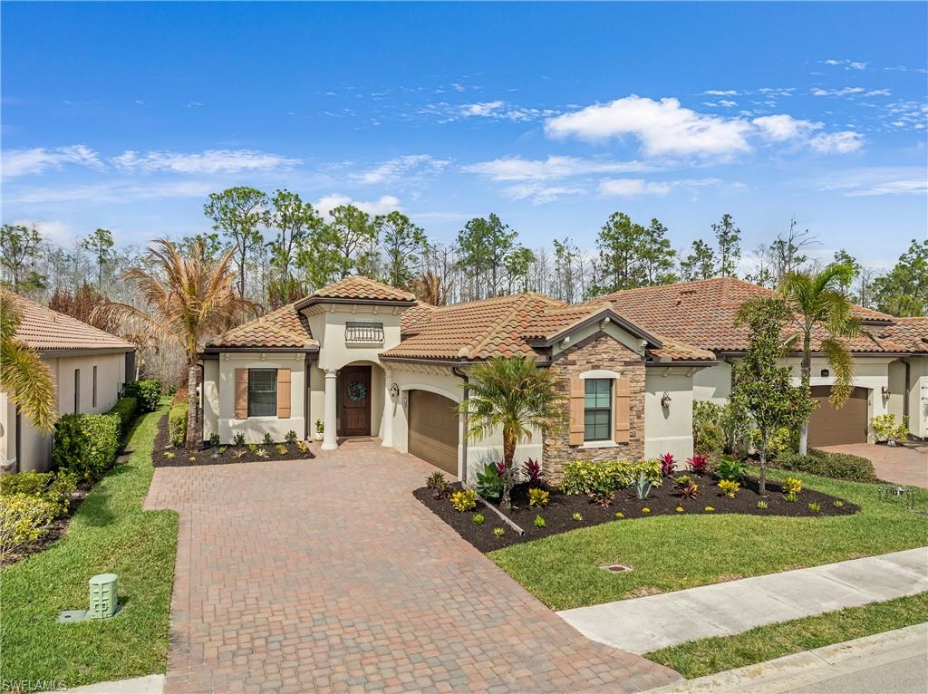 Mediterranean / spanish home featuring stucco siding, stone siding, a garage, driveway, and a front lawn