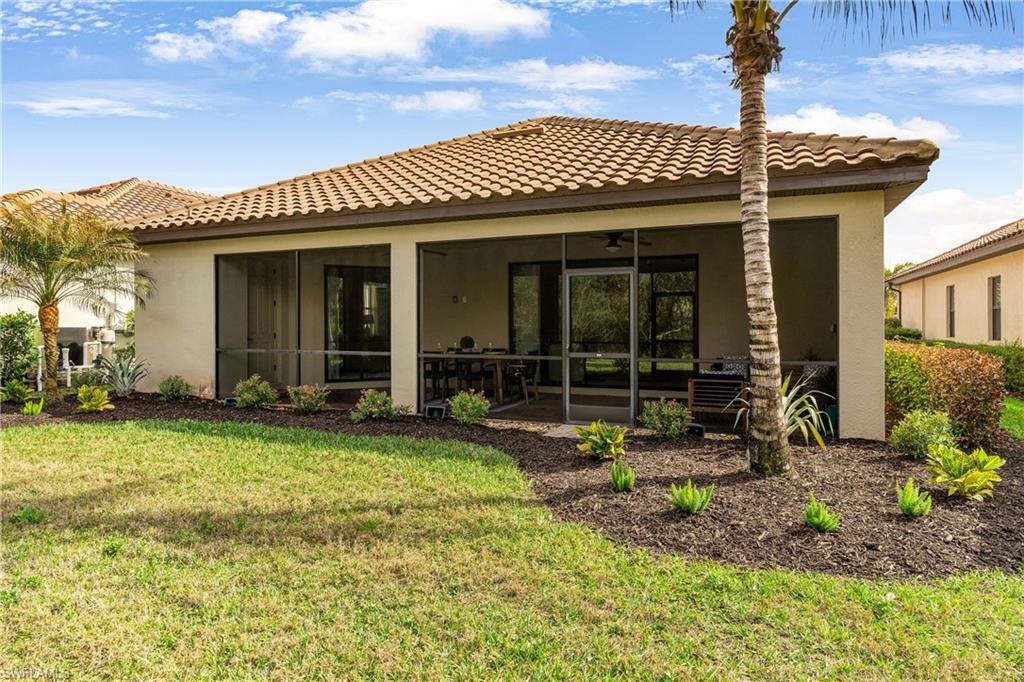 Rear view of property with stucco siding, a tiled roof, a lawn, and a sunroom