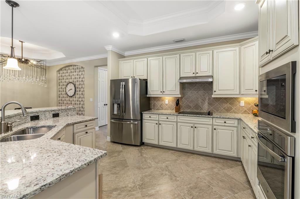 Kitchen featuring a tray ceiling, crown molding, light stone counters, stainless steel appliances, and cream cabinets